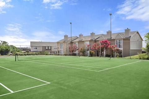 A tennis court is surrounded by apartment buildings.