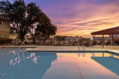 A pool with a tree and a building in the background during sunset.