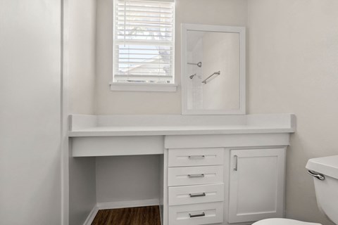 A white bathroom with a window and a mirror.