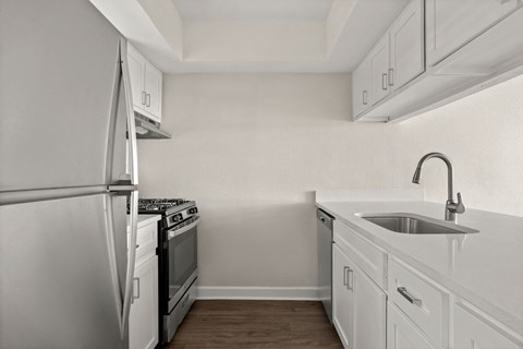 A white kitchen with a refrigerator, stove, and sink.