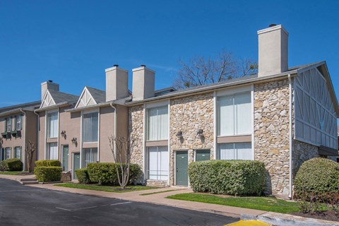 A row of stone and siding townhouses with green doors and bushes in front.