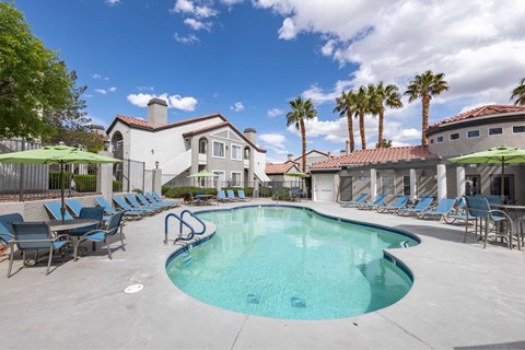 A swimming pool surrounded by lounge chairs and umbrellas with a building in the background.