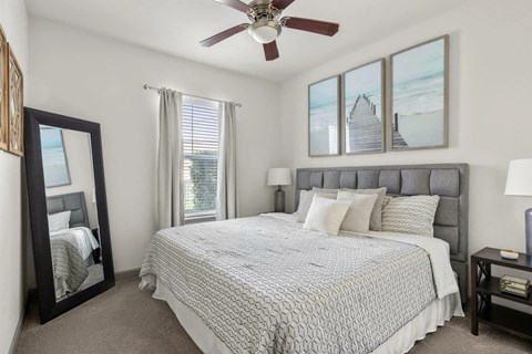 A bedroom with a large bed, a ceiling fan, and a view of a beach through the windows.