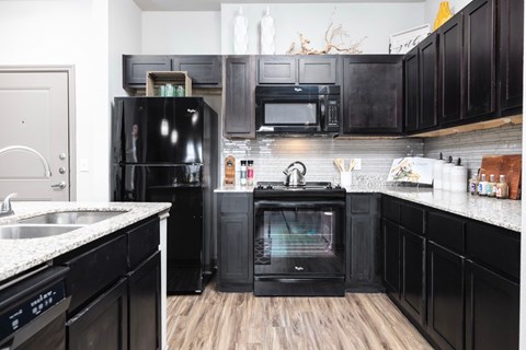 A black fridge and oven in a kitchen with wooden floors.