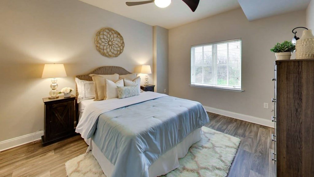 A bedroom with a bed, two lamps, a ceiling fan, and a window.