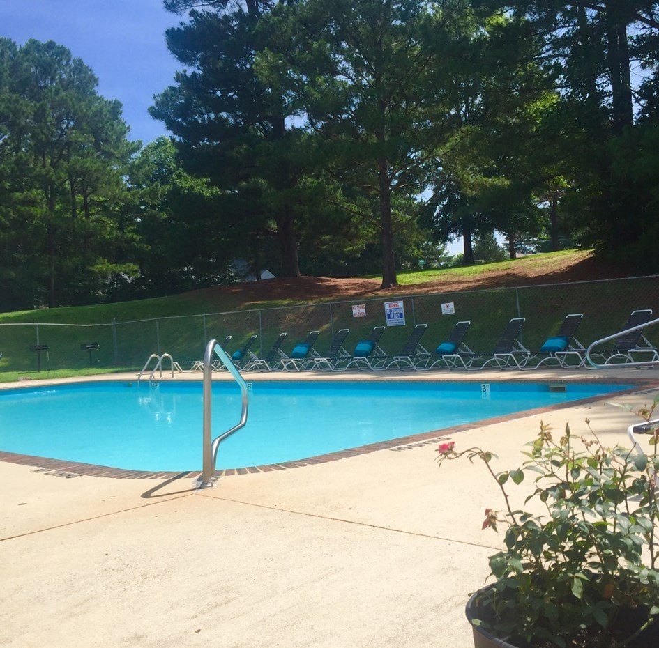 A pool surrounded by trees and chairs.