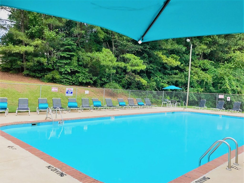 A pool with a blue umbrella and chairs around it.