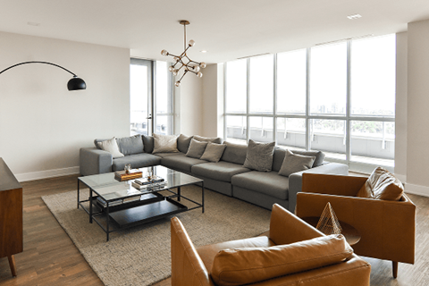 A modern living room with a grey sofa, a glass coffee table, and a large window.