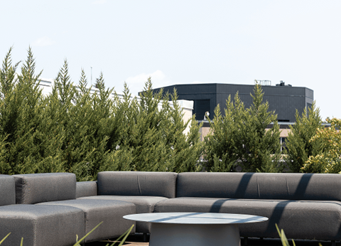 A grey couch with a white table in front of a building and trees.