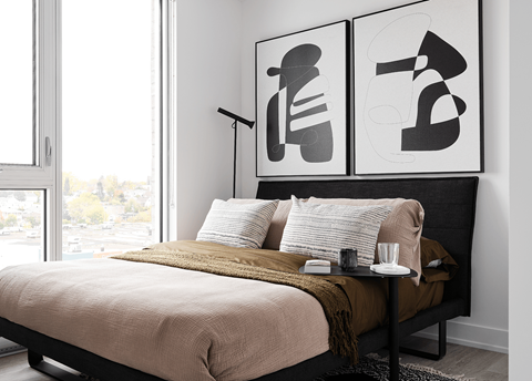 A bedroom with a bed, a table with a glass, a candle, and a plate, and two posters on the wall.