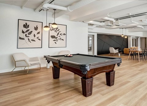 A pool table is in the middle of a room with a chair and a painting on the wall.