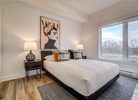 A bedroom with a large bed, a side table with a vase, and a large painting of a woman's face on the wall at Champlain Village Urbain Apartments , Gatineau, J9H 0K9