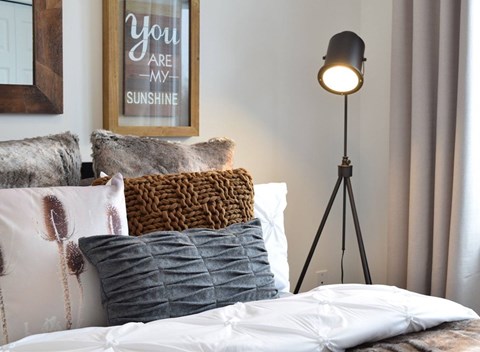 A bedroom with a bed, pillows, a lamp, and a framed picture on the wall.