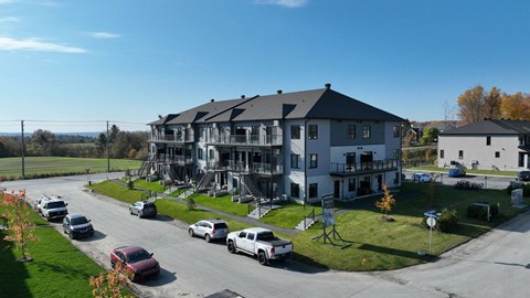 A large white building with a grey roof is surrounded by cars and trees.