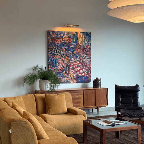 A living room with a yellow couch and a large painting on the wall.