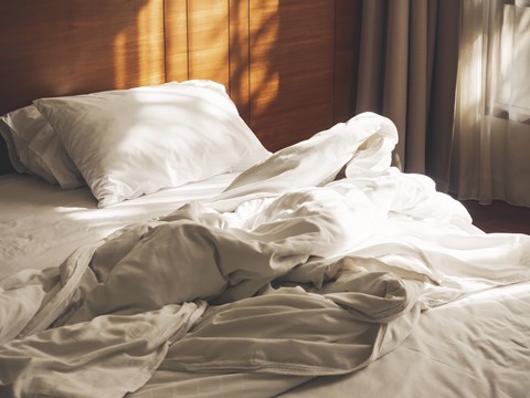 A bed with white pillows and sheets is messy and unmade.