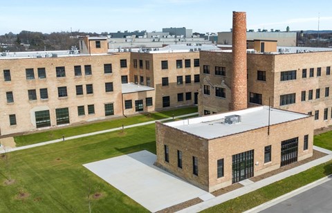 A large brick building with a tall chimney is surrounded by a green lawn.