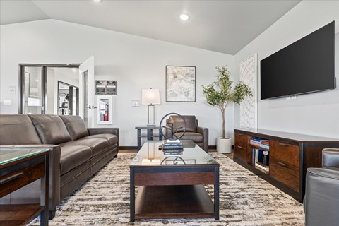 A living room with a brown leather couch, a glass coffee table, and a flat-screen TV mounted on the wall.