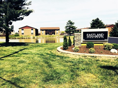 A sign for Eastland Apartments is in the foreground of a grassy area.