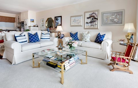 A living room with a white couch, a glass coffee table, and a wooden rocking chair.