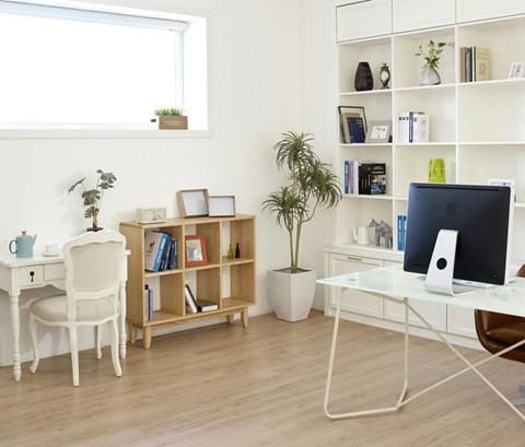A white desk with a computer and a chair in front of a window with a shelf and potted plant.