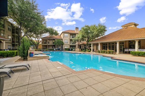 A swimming pool surrounded by a tiled patio and buildings.