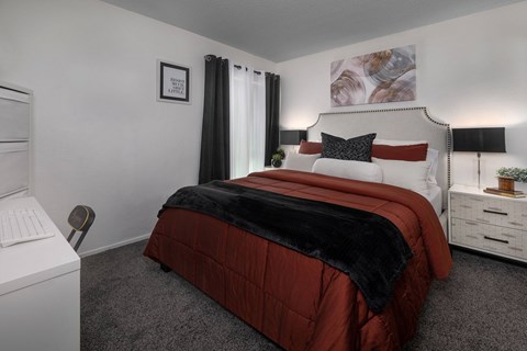 A bedroom with a red comforter and a white nightstand.