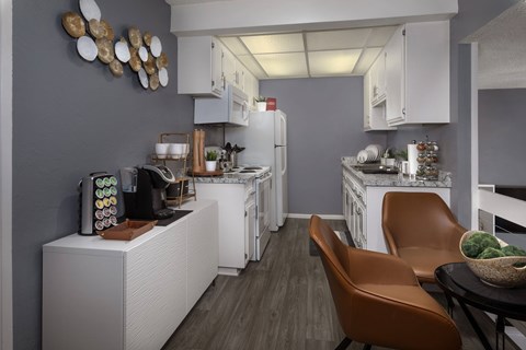 A modern kitchen with white appliances and brown leather chairs.