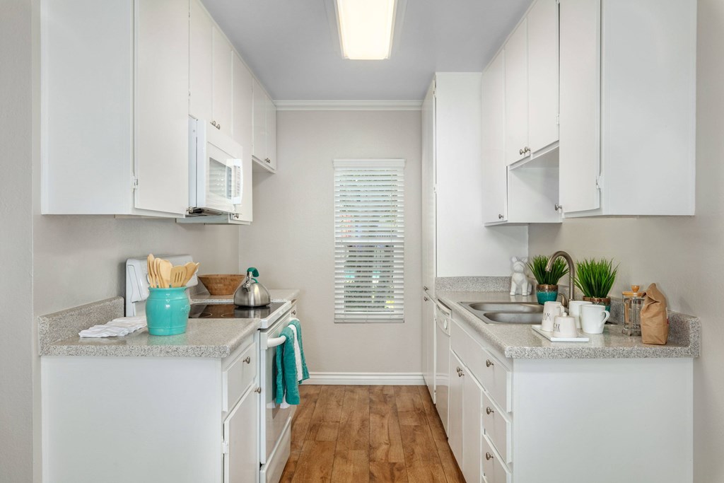 A kitchen with white cabinets and a window on the wall near the refridgerator.