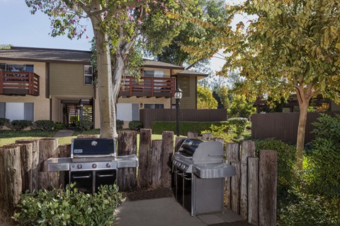 A BBQ grill is in the middle of a yard with a building in the background.