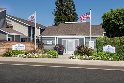 The leasing office with Carmenita Townhouse Apartments signs surrounded by flowers and greenery out front.
