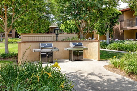 Two BBQ grills are situated on a concrete platform in a grassy area.