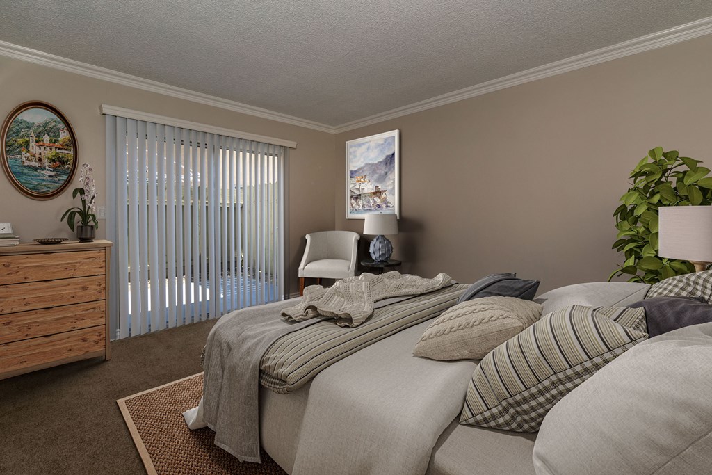 A bedroom with a bed, pillows, a nightstand, a plant, and a window with blinds.