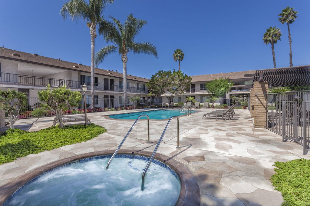 A pool with a slide in the middle of a courtyard surrounded by palm trees.