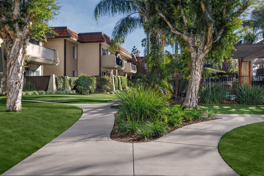 A concrete walkway leads through a landscaped area in front of apartment buildings.