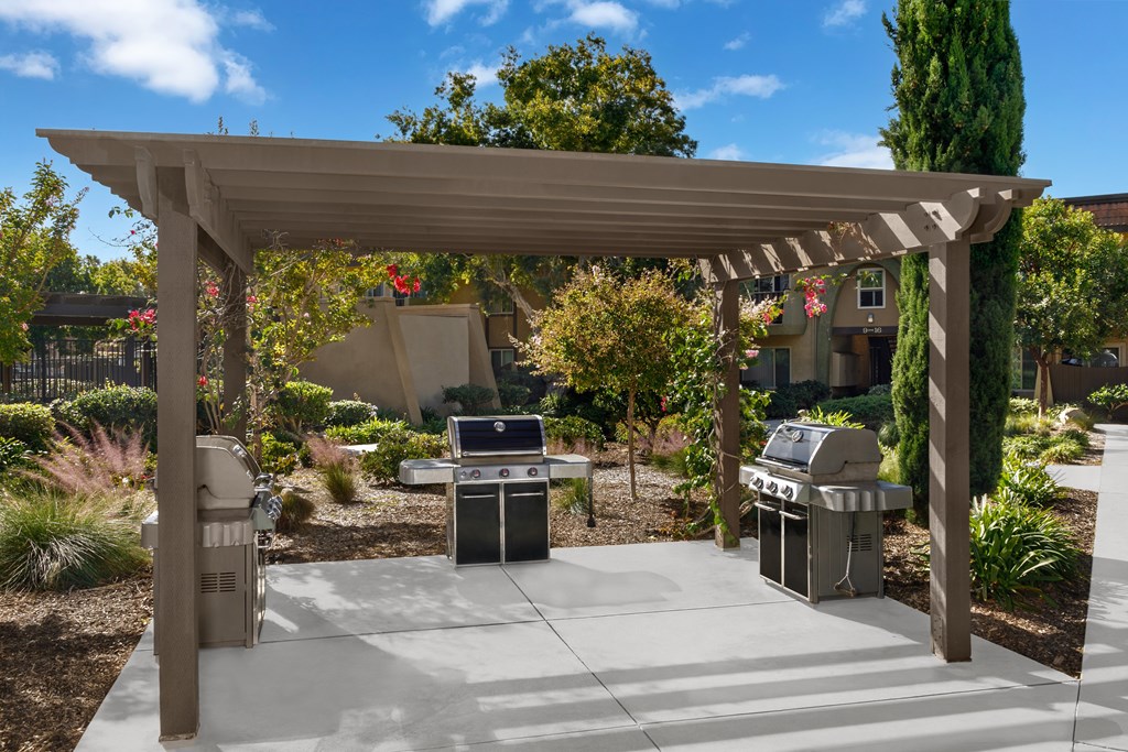 A patio with a grill and a pergola.