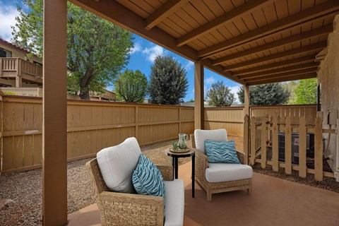 A patio with a wicker chair and a small table with a green cup on it.