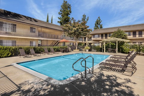 A swimming pool surrounded by lounge chairs and umbrellas in a sunny day.