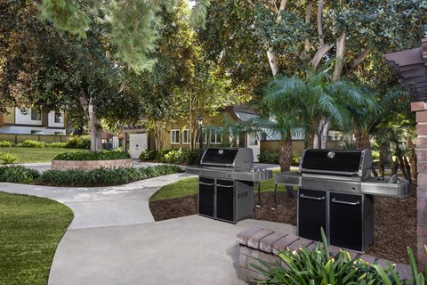 Two grills in a barbeque area located in a landscaped yard.