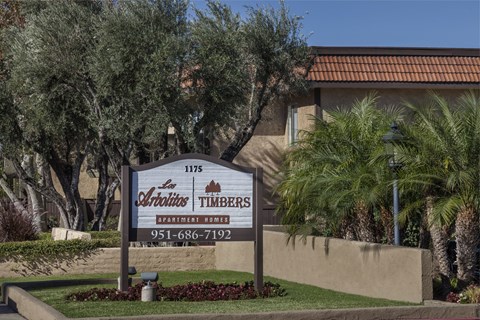 A sign for Timbers Apartment Homes in front of some palm trees.