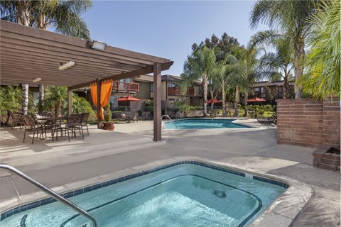 A pool and jacuzzi with a patio with chairs and a table.