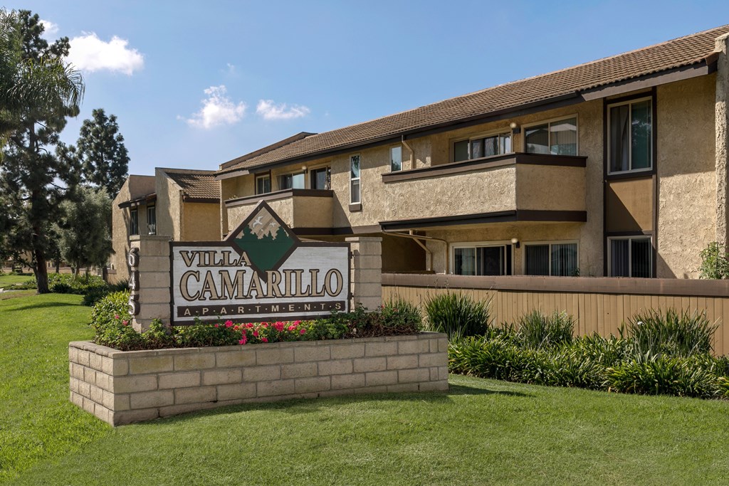 A sign for Villa Camarillo Apartments is in front of a tan building.