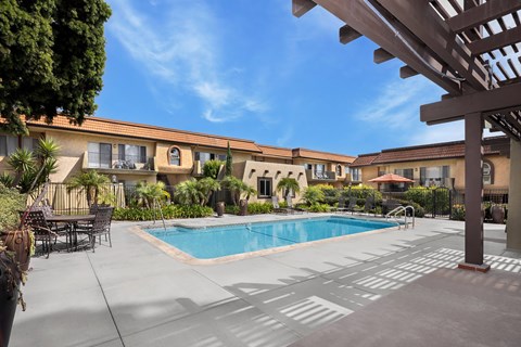 A pool area with a table and chairs and a building in the background.