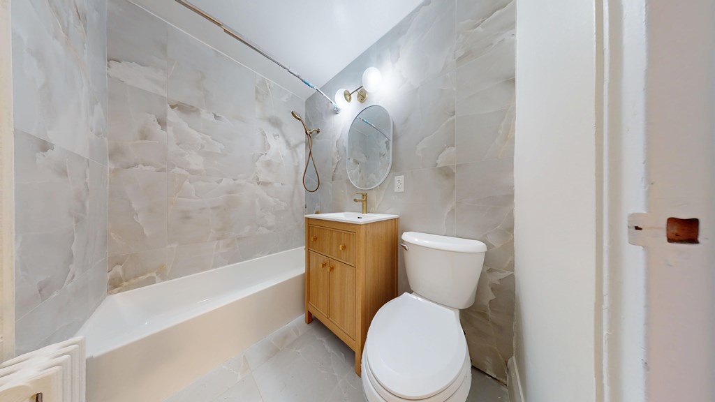 A white toilet sits in a bathroom with a marble wall.