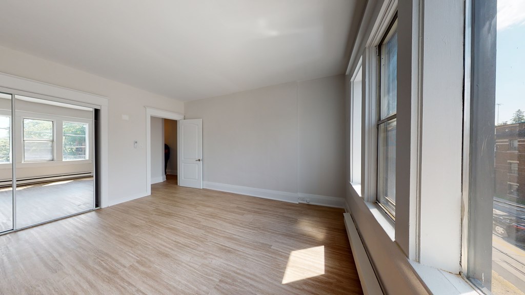 A room with wooden floors and white walls, with a view of the outside through large windows.