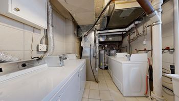 A white washing machine is in a laundry room with a dryer and a washing machine in the background.