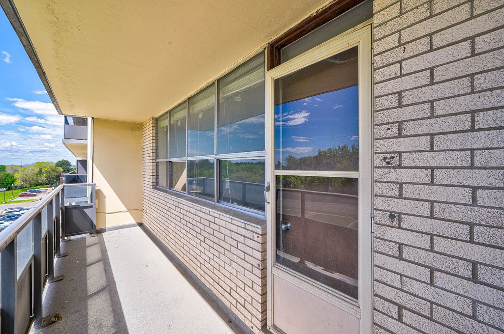 A balcony with a brick wall and a window overlooking a tree-filled landscape.