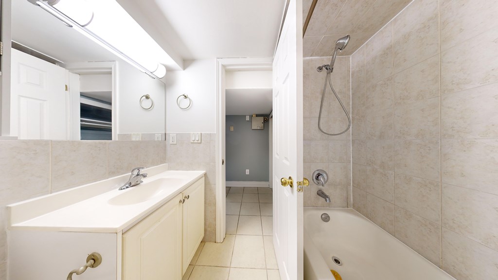 A white bathroom with a sink, mirror, and bathtub.