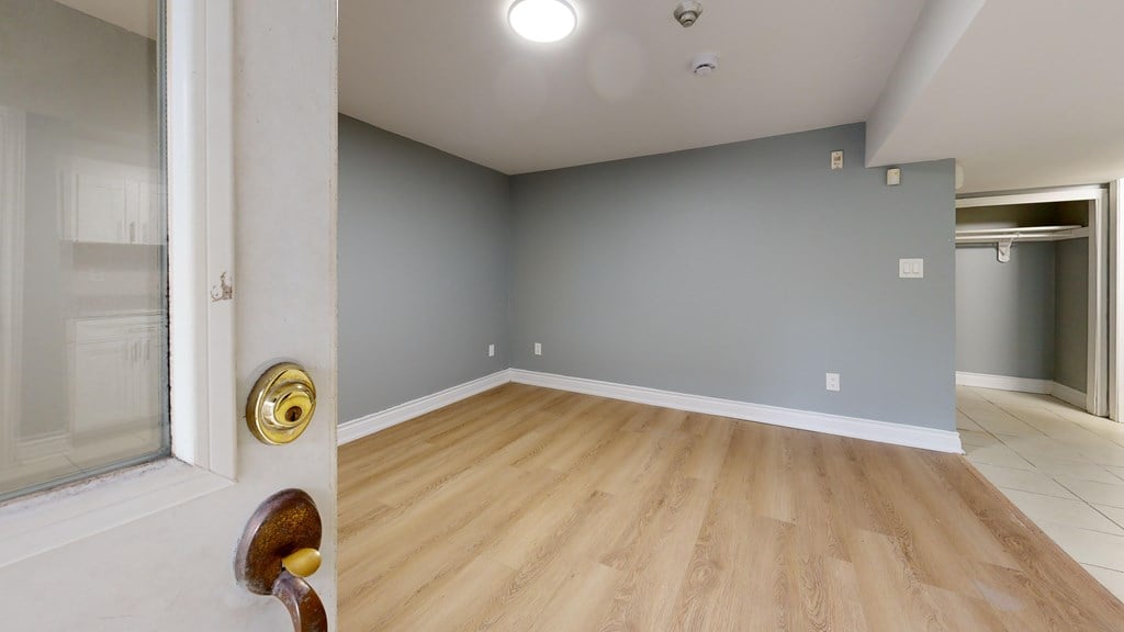A room with wooden flooring and a white door with a gold handle.