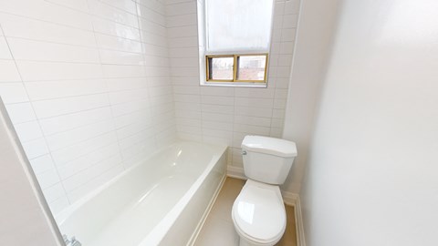 A white toilet sits next to a bathtub in a bathroom with white tiles.